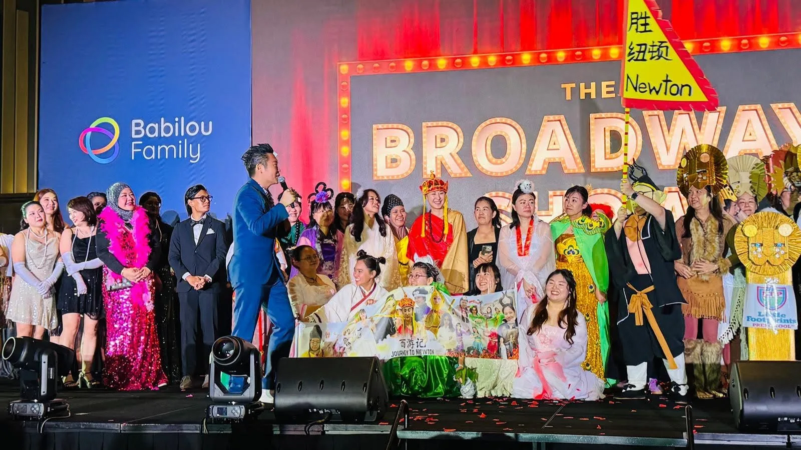 James Yang hosting The Broadway Show for Babilou Family, the cast in costume behind him