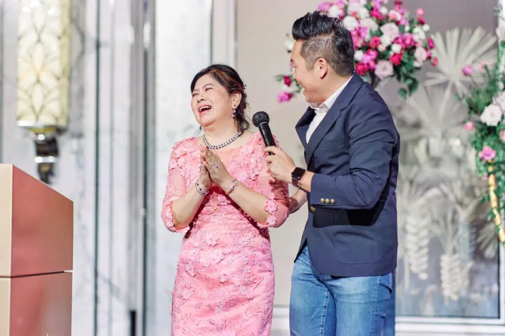 James Yang hosting on stage at a wedding, a guest laughing beside him